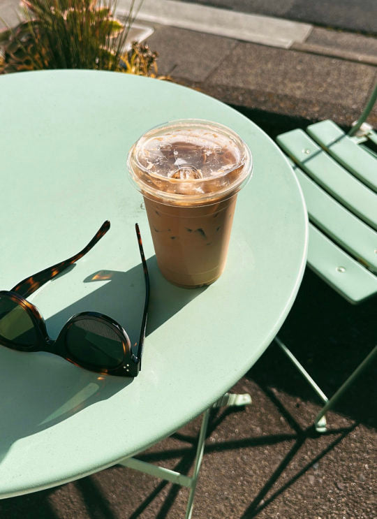 Grüner Gartentisch mit Iced-Kaffee und Sonnenbrille